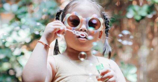 child wearing flower sunglasses blows bubbles