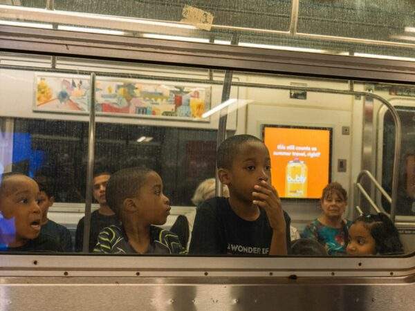 three young black boys look out the window of a subway car