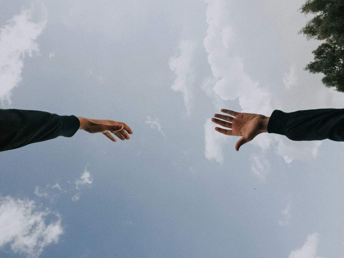 two hands reaching out to each other across a cloudy sky
