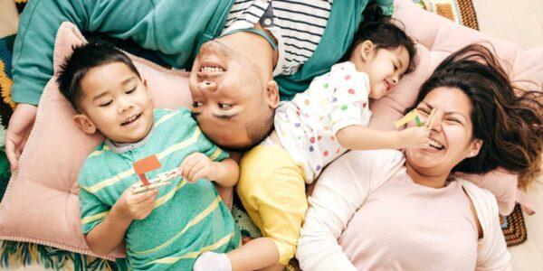 family of four laughing and playing on rug with pillows