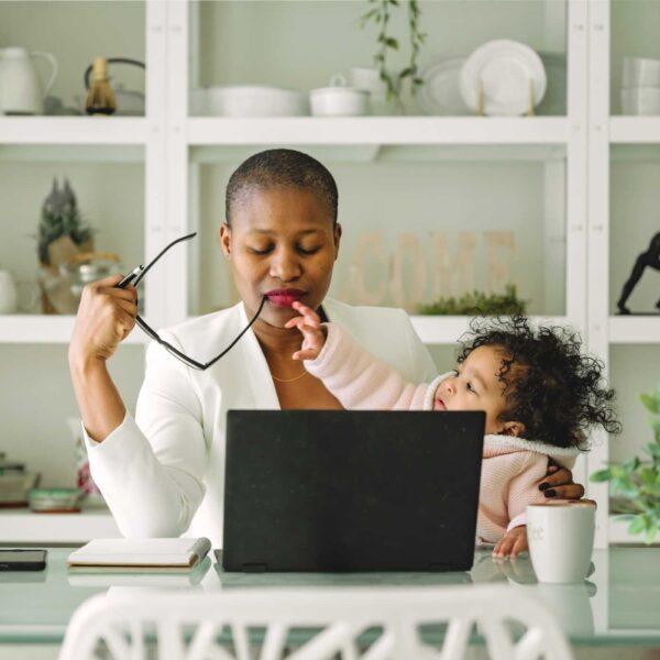 Baby reaching for mother's glasses as she works on a laptop, eyes closed