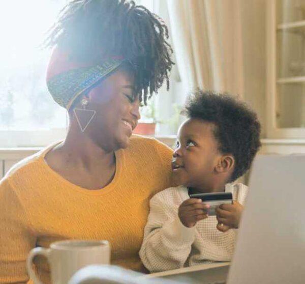 happy mother working at her laptop smiles at her child backlit by sunny window